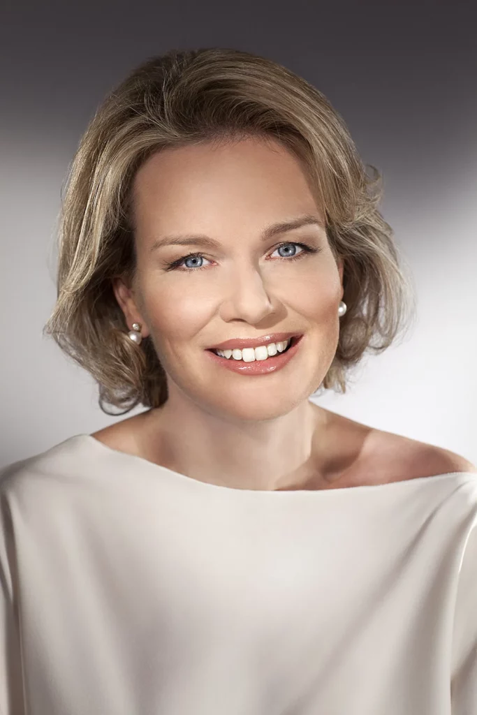 Portrait serré de la Reine Mathilde, expression très souriante et lumineuse.