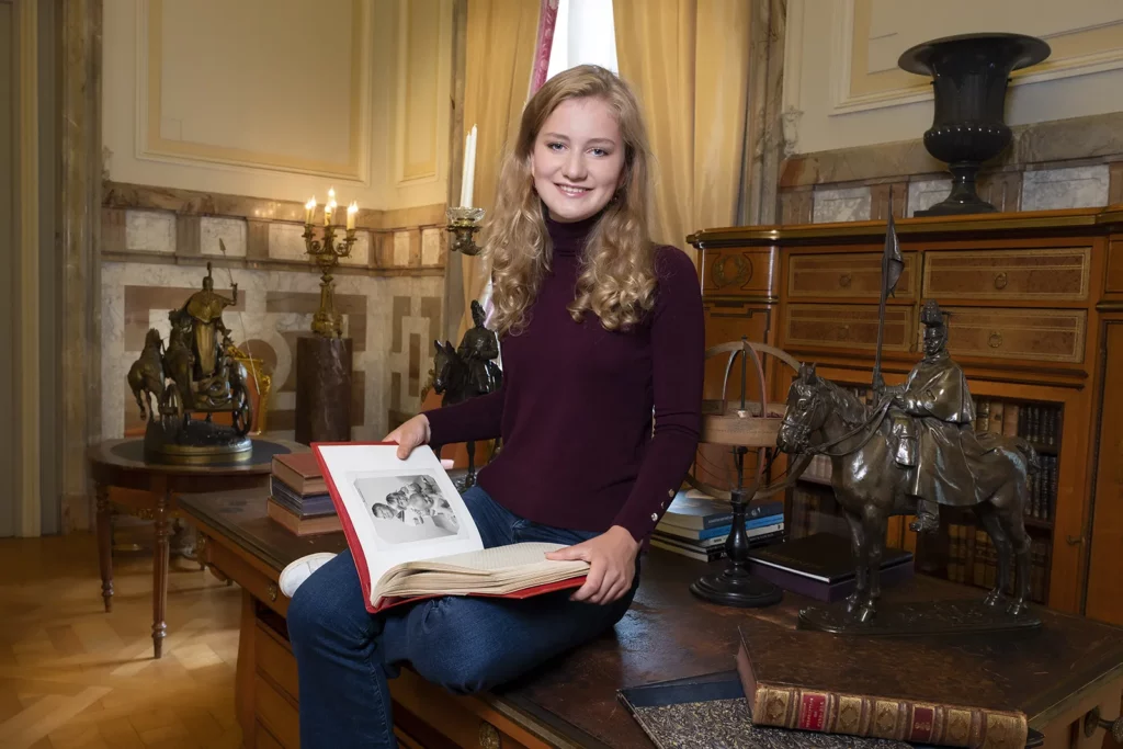 Princesse Elisabeth de Belgique décontractée sur un bureau historique avec un album photo de famille.