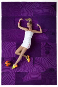 Emilie Dupuis en tenue de sport blanche et chaussures fluo, shootant dans un ballon orange sur un tapis fuchsia.