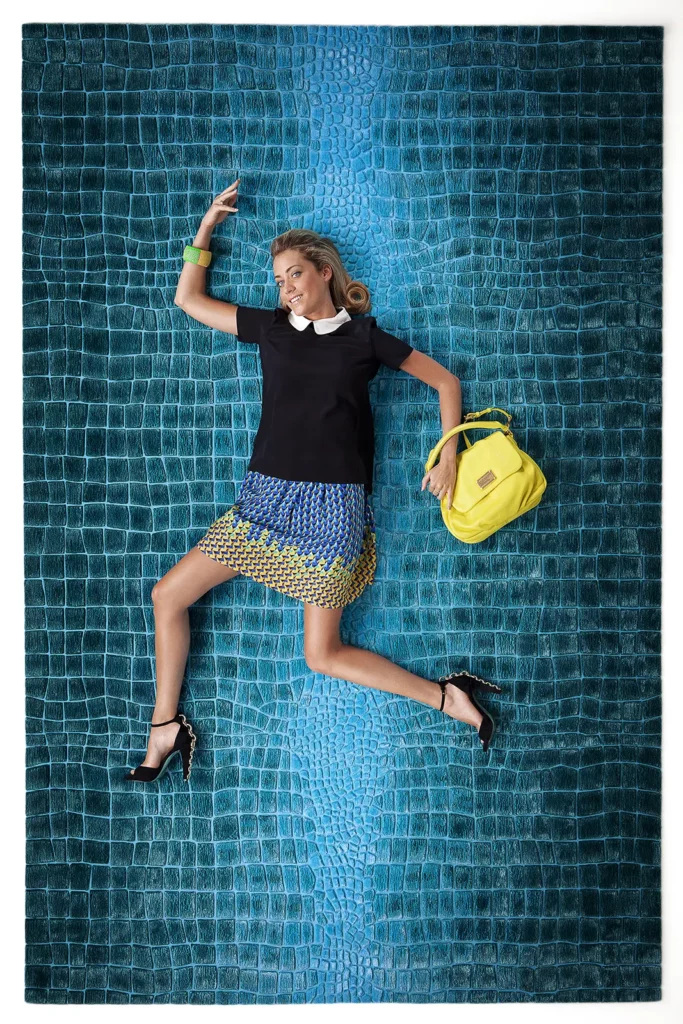 Emilie Dupuis sur un tapis Crocodeluxe bleu de Floor To Heaven avec un sac jaune vif en contraste.