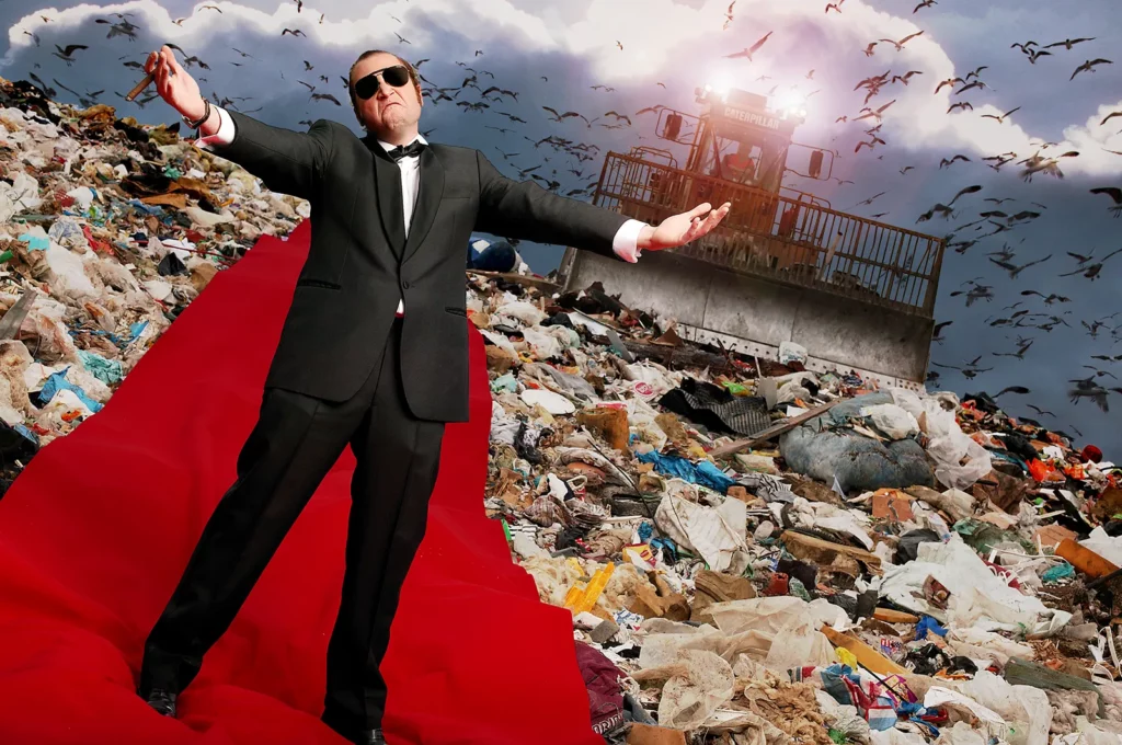 Portrait décalé de François Damiens en smoking sur un tapis rouge dans un décor industriel atypique.