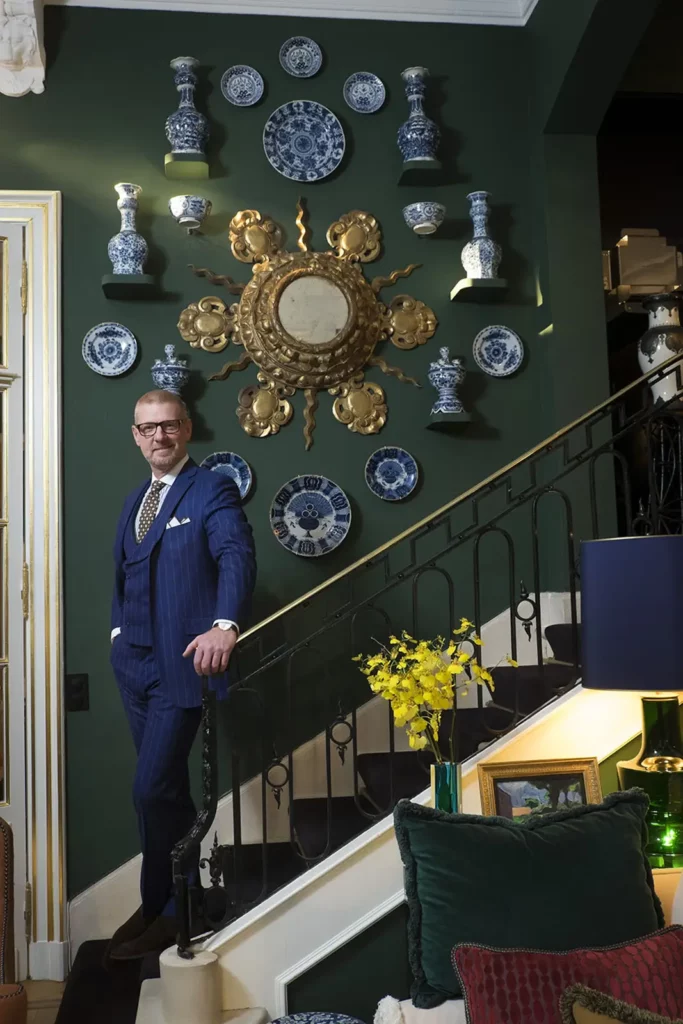 Gérald Watelet en costume trois pièces bleu sur l'escalier de son appartement bruxellois.