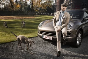 Gérald Watelet en tenue gentleman farmer appuyé sur une Porsche Cayenne champagne avec des chiens Braque de Weimar.