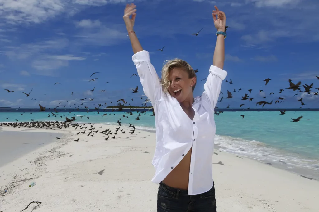 Julie Taton souriante sur un banc de sable aux Maldives, shooting mode au Kanuhura pour Paris Match.