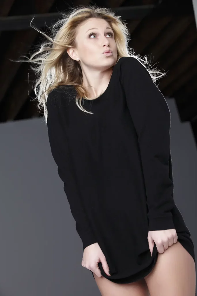 Julie Taton en pull noir en studio, faisant la moue et regardant sur le côté, avec un effet de halo lumineux.