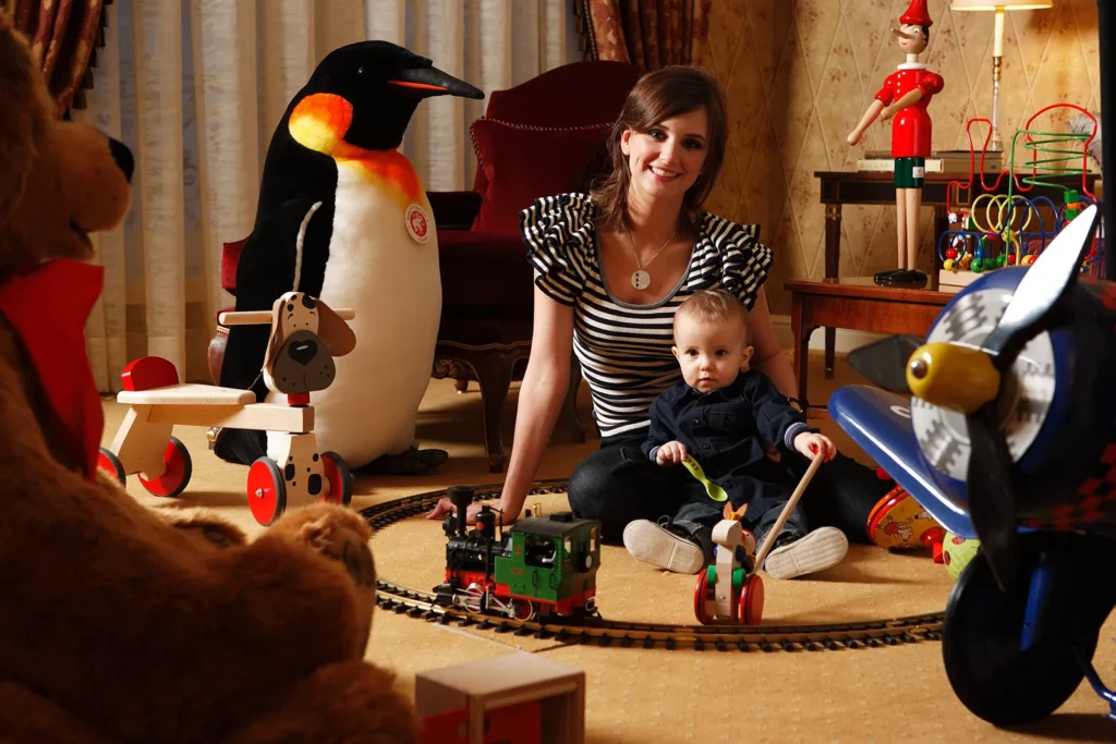 Elodie De Sélys jouant avec son fils Côme sur le tapis de la suite Royale avec des jouets Serneels.
