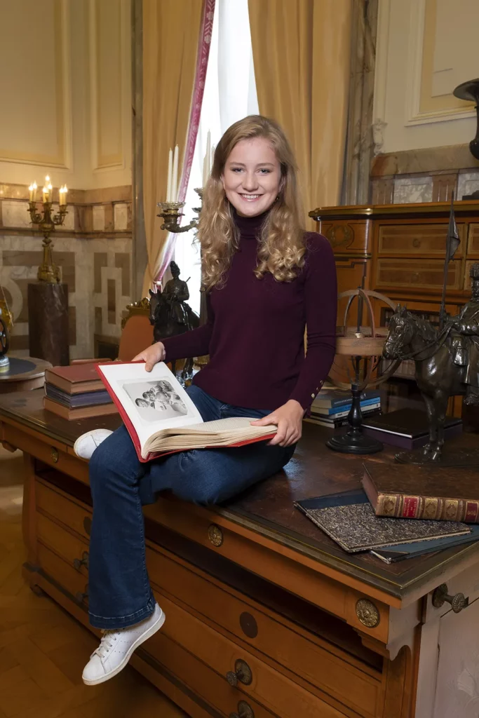 La Princesse Elisabeth assise sur un bureau d'époque au Château de Laeken, regardant un album de famille.