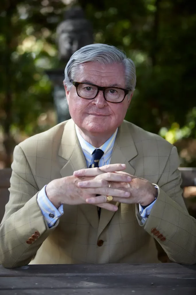 Portrait de l'avocat Xavier Magnée dans son jardin, assis les mains croisées, regardant l'objectif. Photographie de Marc Gronemberger.
