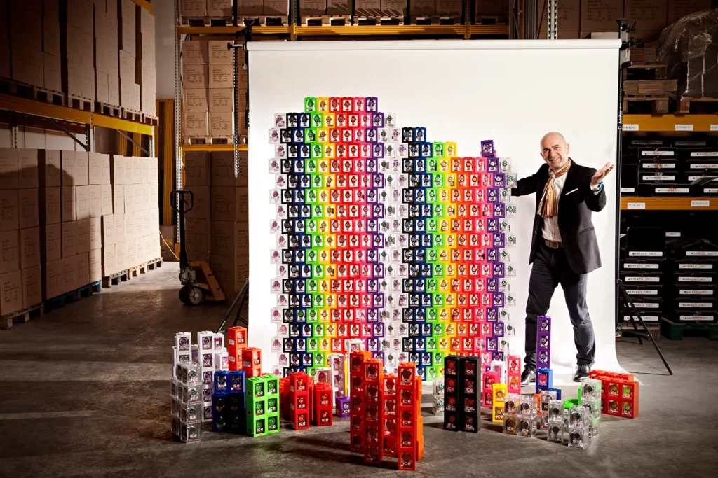 Jean-Pierre Lutgen, CEO d'Ice-Watch, posant devant un mur de boîtes de montres assemblées dans son entrepôt à Bastogne.