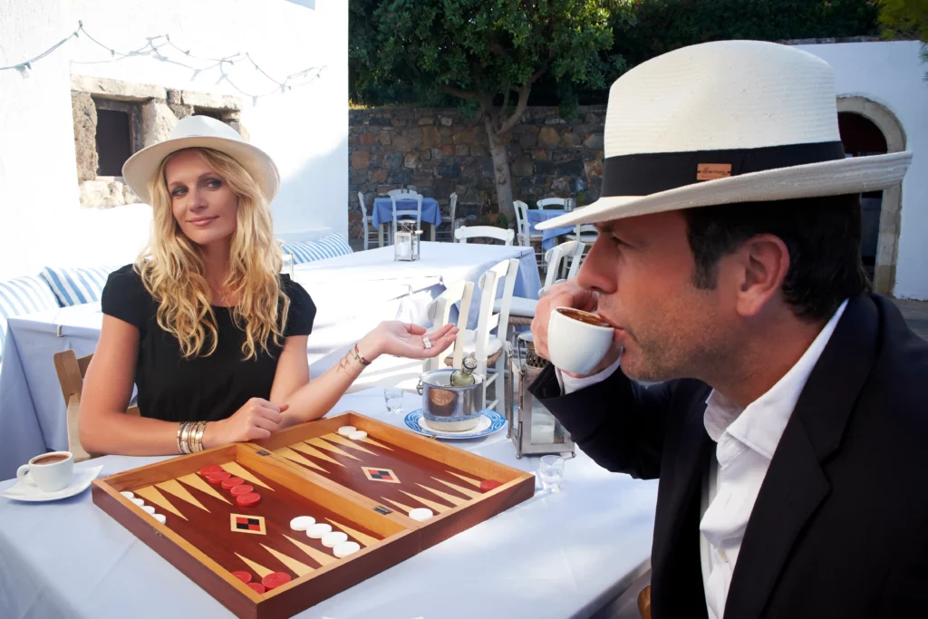 Sandrine Corman et Michel Bouhoulle jouant au backgammon en terrasse, portant des chapeaux Panama Herman Headwear.