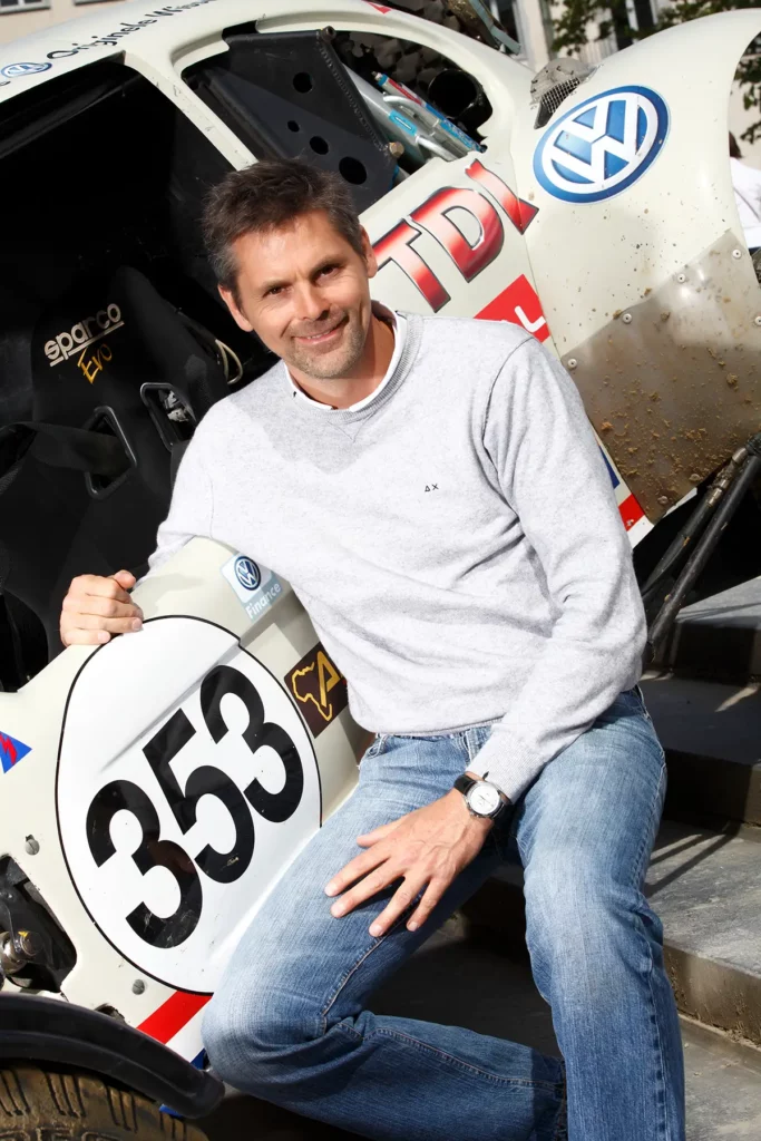Portrait de Stéphane Henrard en plan américain, appuyé contre son Buggy VW. Photographie professionnelle par Michel Gronemberger à Bruxelles.