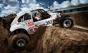 Vanina Ickx au volant du Buggy de Stéphane Henrard sur une dune de sable à Hoeilaart (travaux RER). Un train file en arrière-plan. Photographie d'action par Michel Gronemberger.