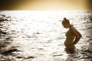 Silhouette en contre-jour de Julie Taton enceinte dans la mer à l'île Maurice, regardant son ventre en fin de journée.