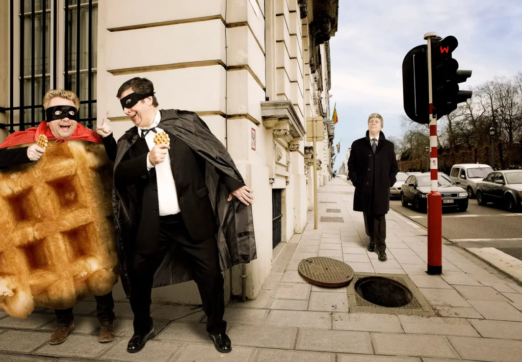 Votez pour moi : Wafelman et Suzyx piégeant Didier Reynders avec une bouche d'égout ouverte rue de la Loi.