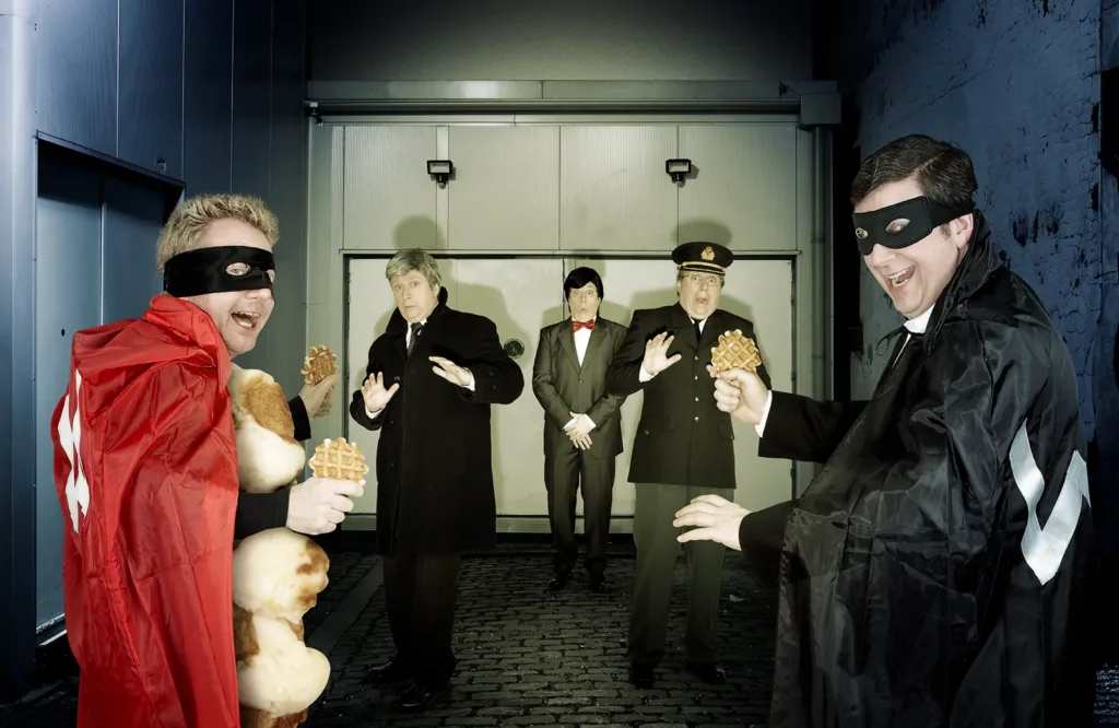 Votez pour moi : Wafelman et Suzyx menaçant avec des gaufres le Roi Albert II, Elio Di Rupo et Didier Reynders dans une impasse.