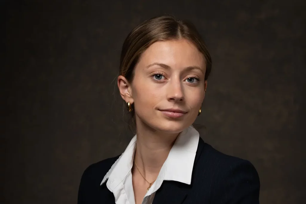 Photo de CV professionnel au format horizontal d'une jeune femme légèrement souriante en veston noir et chemise blanche en studio.