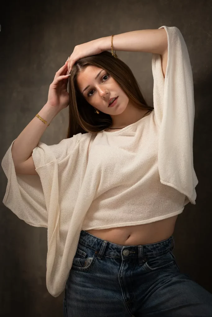 Photographe book modèle Bruxelles, jeune femme posant de face les deux mains sur la tête avec un top blanc fluide à manches larges.