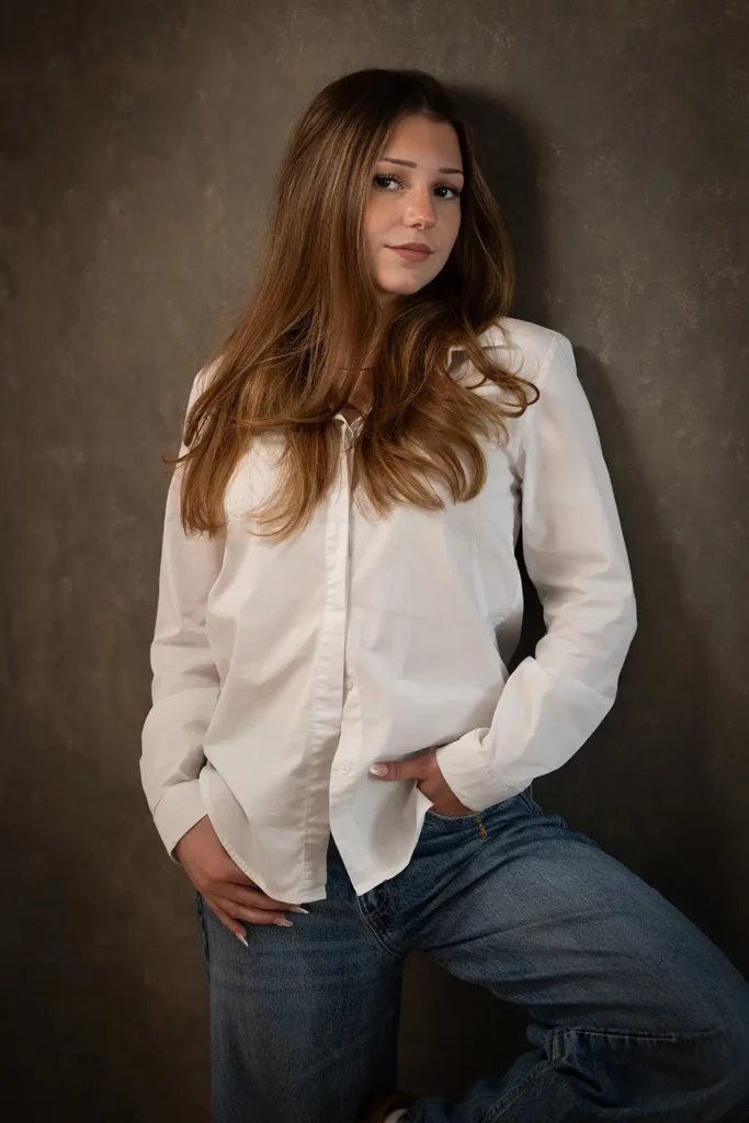 Photographe book modèle Bruxelles, shooting professionnel d'une jeune fille en chemisier blanc et jeans sur fond de studio gris texturé.