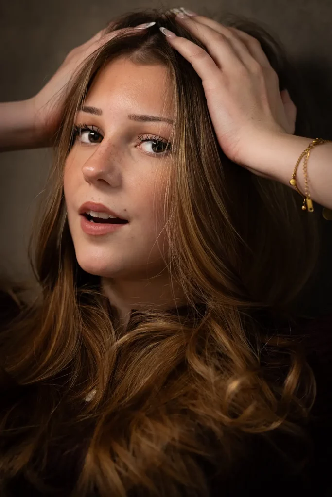 Photographe book modèle Bruxelles, portrait en gros plan d'une jeune fille aux cheveux bouclés posant les deux mains sur la tête.