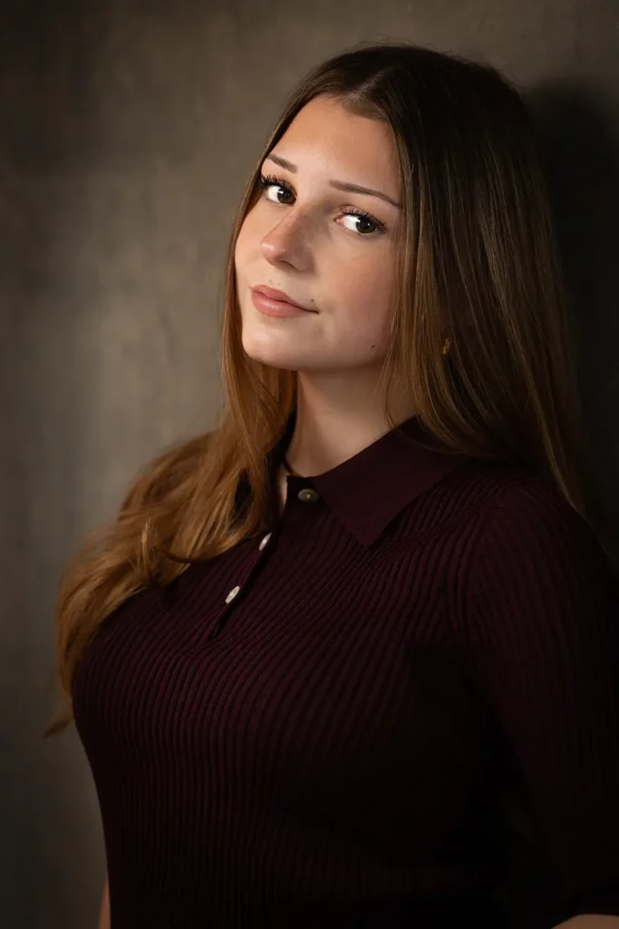 Photographe book modèle Bruxelles, portrait de profil trois-quarts d'une jeune fille en top bordeaux avec un léger sourire.
